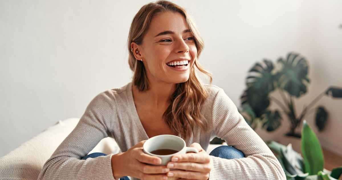 A young woman with a cup of hot coffee or tea is sitting on a sofa. (Representative Cover Image: Getty Images | Valerii Apetroaiei.)