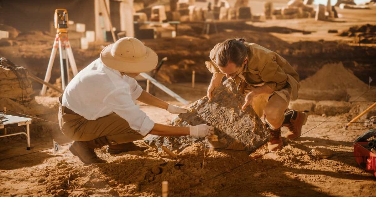 Two archeologists work on an excavation site, cleaning and lifting newly discovered ancient civilization's artifacts. (Representative Cover Image Source: | Pho