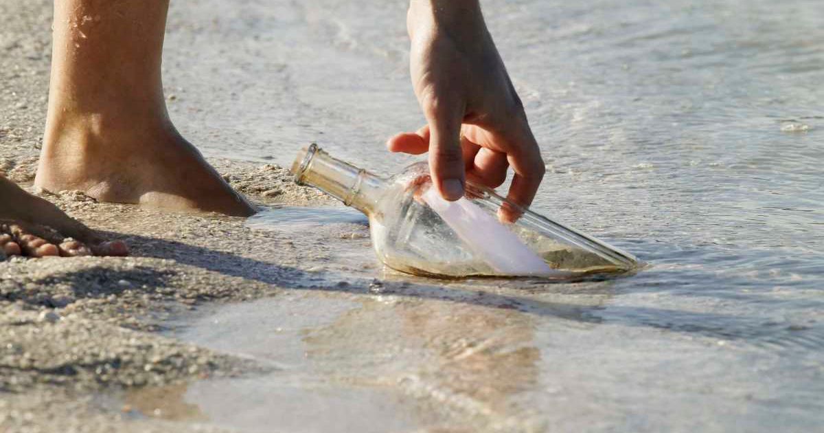 A man picking up a message in a bottle lying on the beach. (Representative Cover Image Source: Getty Images | Photo by Burazin)