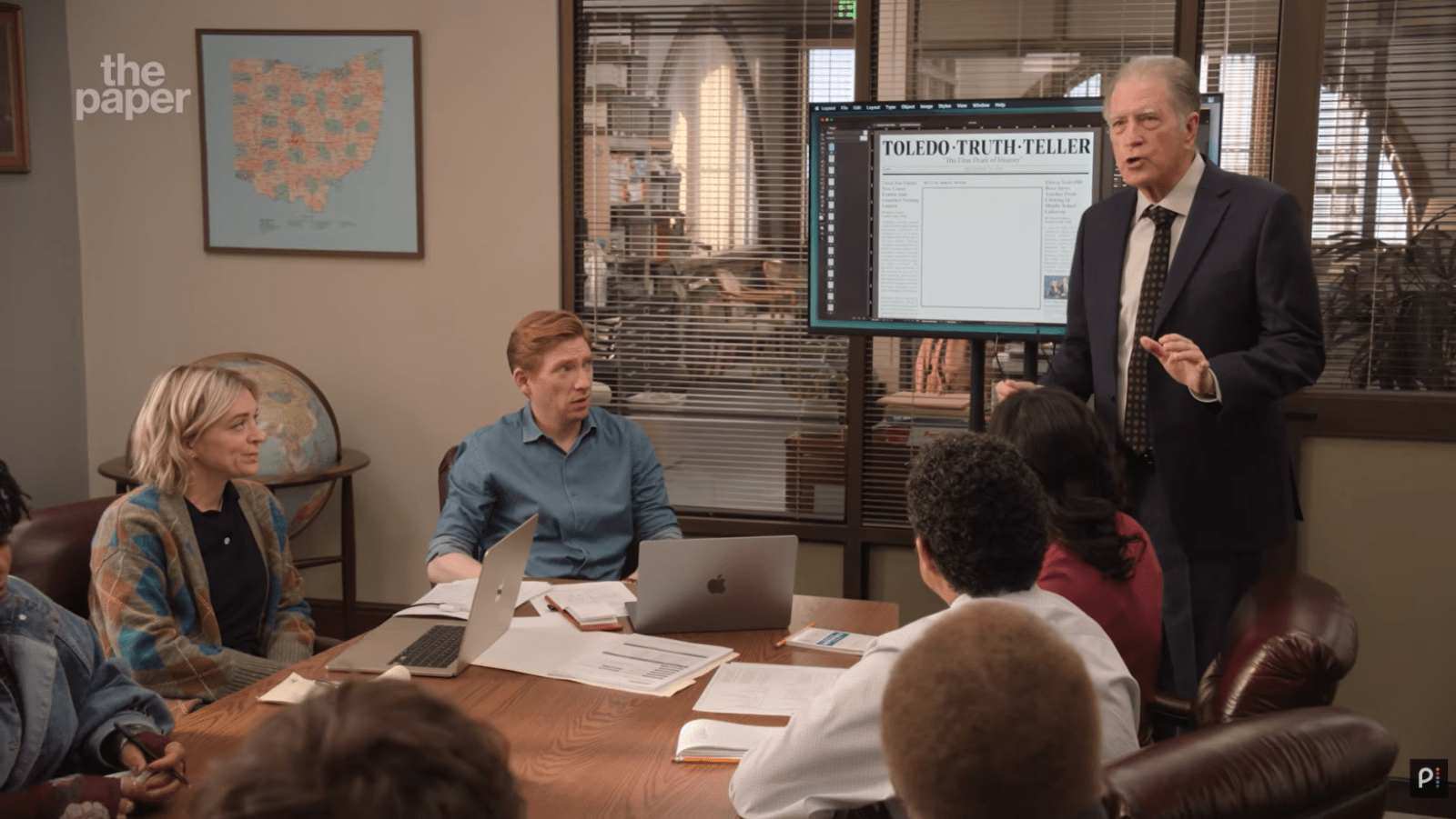 The Toledo Truth Teller staff attend a newsroom meeting in ‘The Paper’ Season 2 (Cover Image Source: YouTube | Peacock)