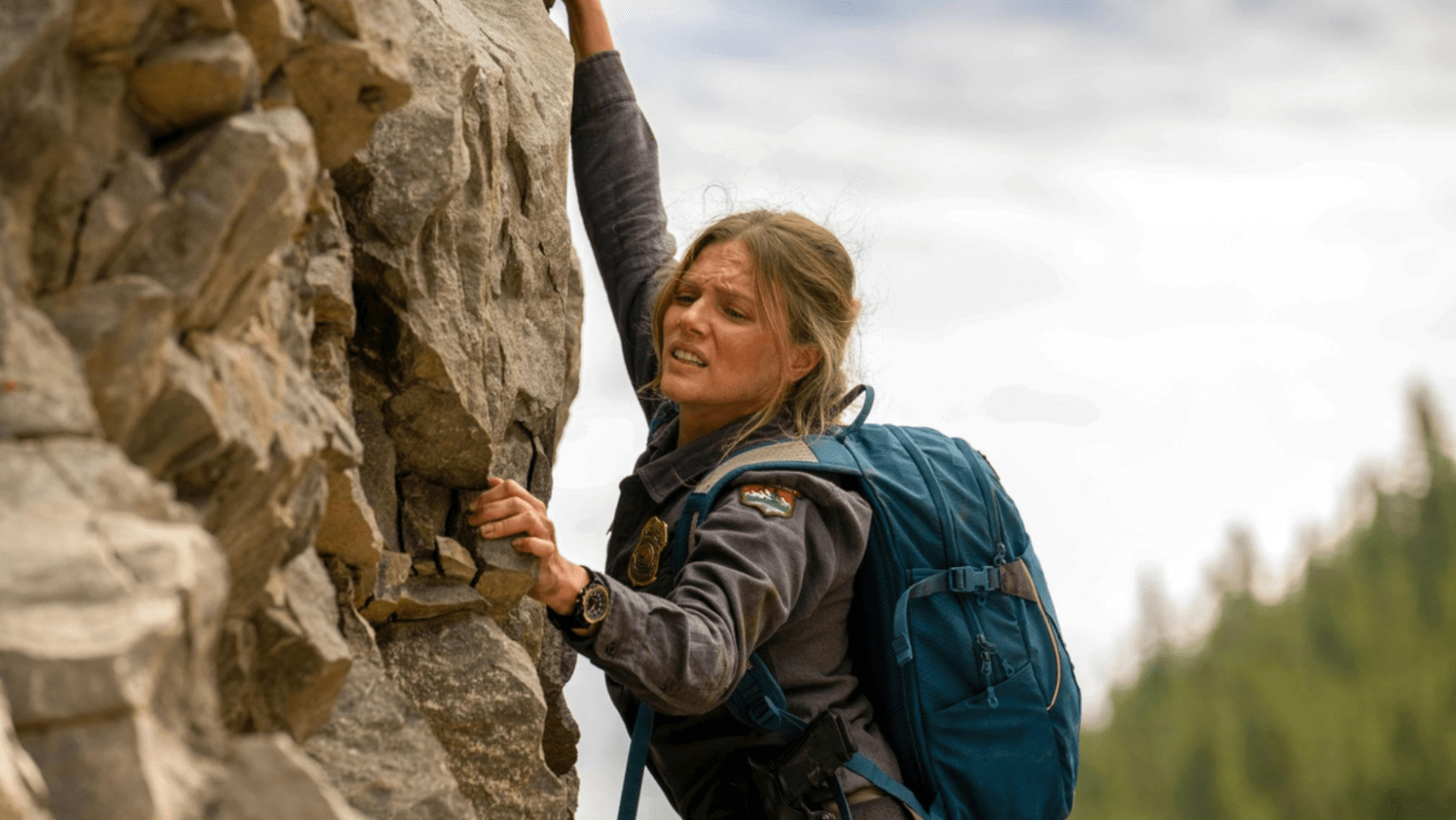 Tracy Spiridakos as Anna Pigeon climbs a rocky cliff in ‘Anna Pigeon’ (Image Source: Michelle Faye/USA Network)