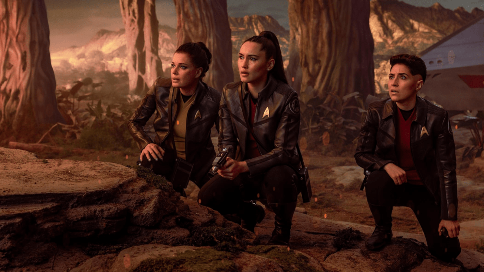 Rebecca Romijn as Una Chin-Riley, Christina Chong as La’an Noonien-Singh and Melissa Navia as Erica Ortegas crouch together on an away mission in ‘Star Trek: Strange New Worlds’ Season 4 (Image Source: Jan Thijs/Paramount+)