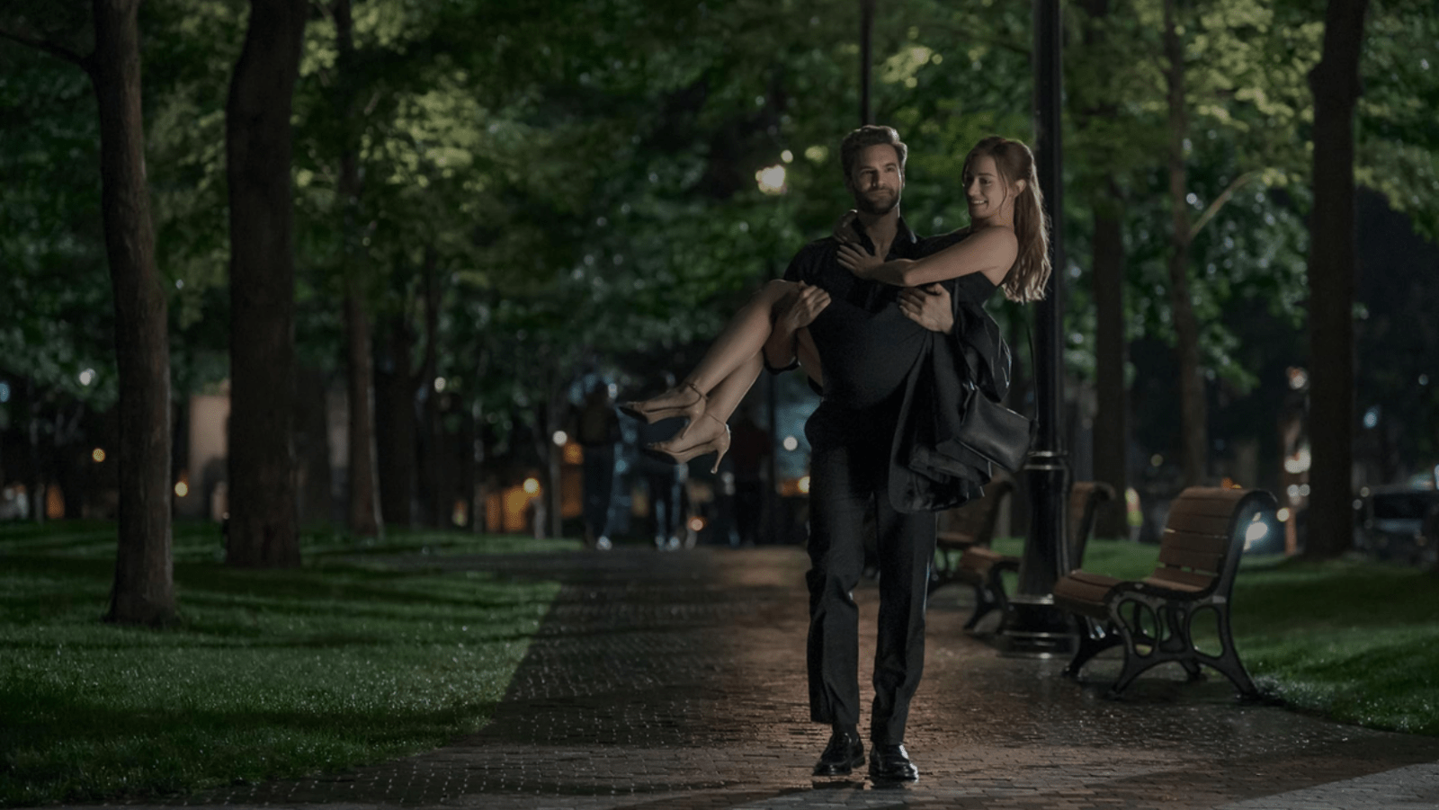 Adam Carlsen (Tom Bateman) carries Olive Smith (Lili Reinhart) through a park at night (Image Source: Prime Video | Youtube)